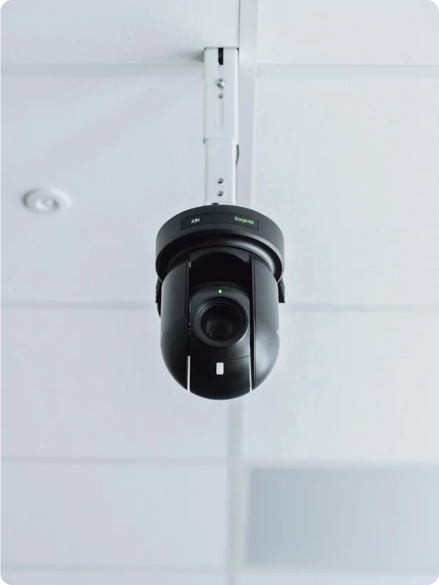 Et svart kamera som henger fra taket i et klasserom. Bildet er close up.